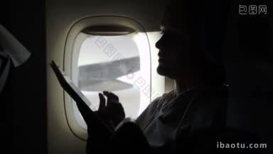 在<strong>飞机</strong>上，一位女士坐在照明灯旁，在平板电脑上打字